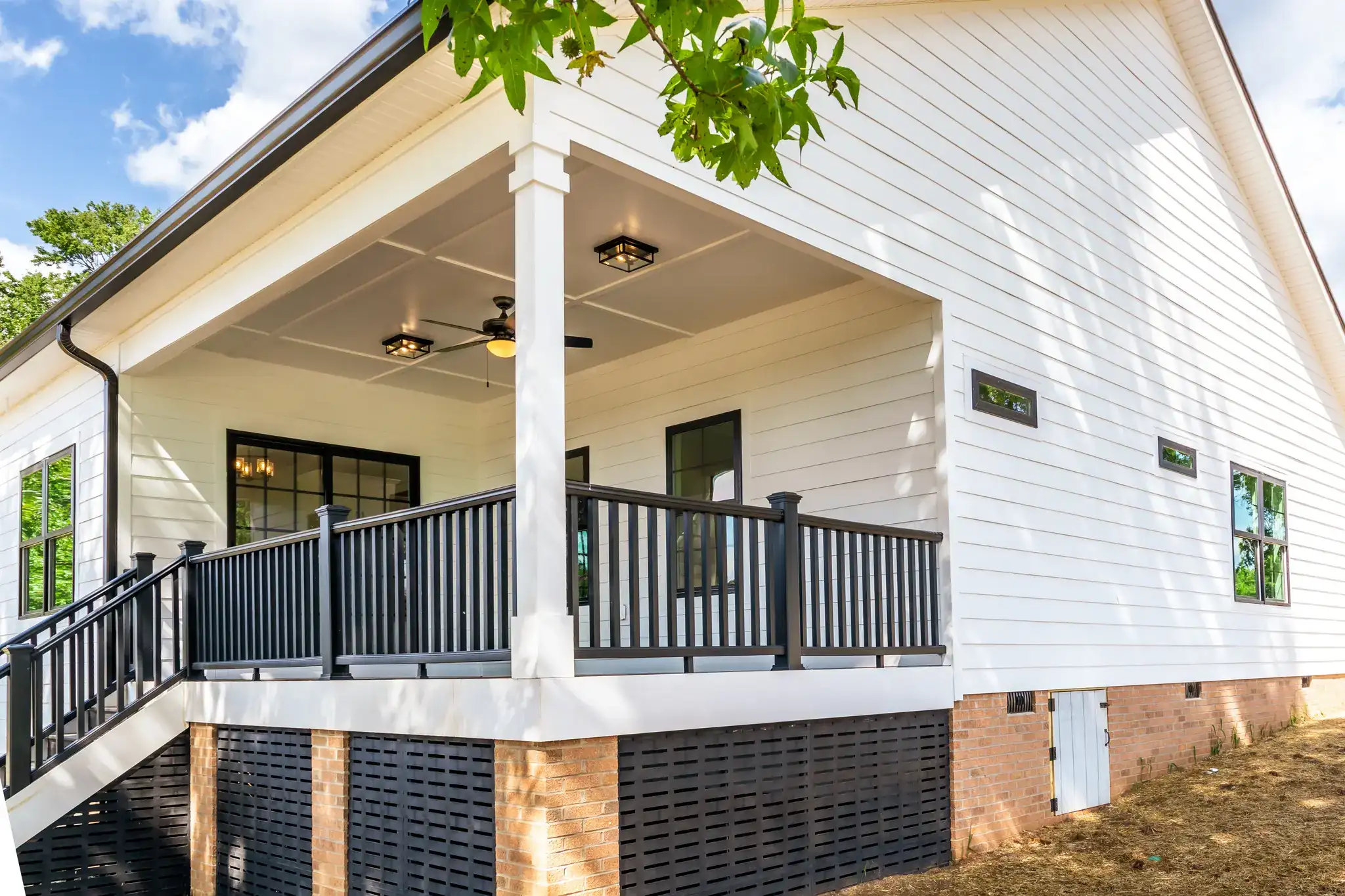 Custom home covered front porch with a white column, black railing and ceiling fan