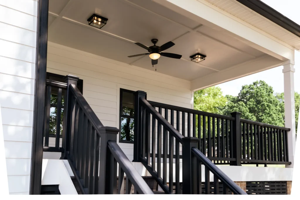 Covered porch of a custom home with black railings, columns and a ceiling fan