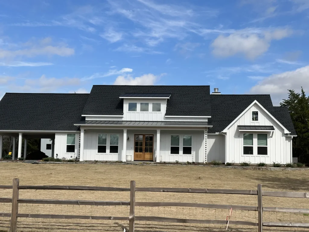 Custom-built white modern farmhouse with a dark metal roof and split-rail fencing