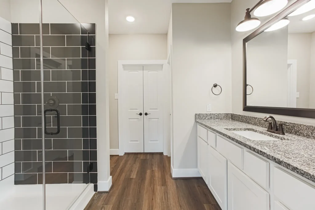 Custom home bathroom with white closet doors, a tile accent wall and wood-look flooring