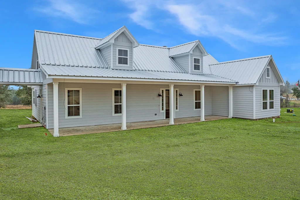 Custom-built white farmhouse with a metal roof and a full-length covered front porch