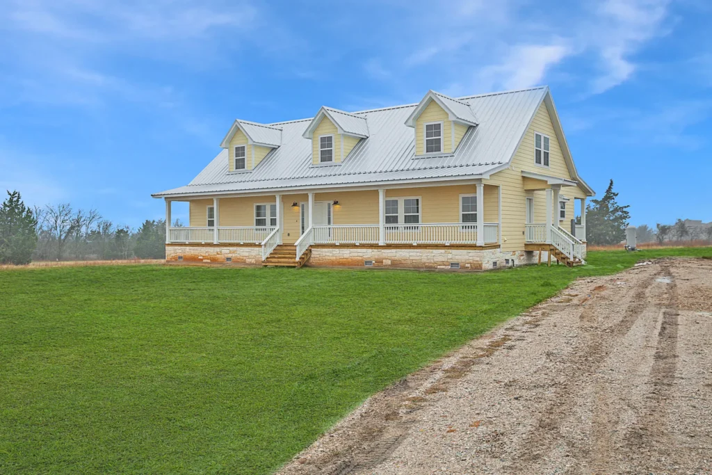 Custom-built white two-story farmhouse with dormers and a gravel driveway