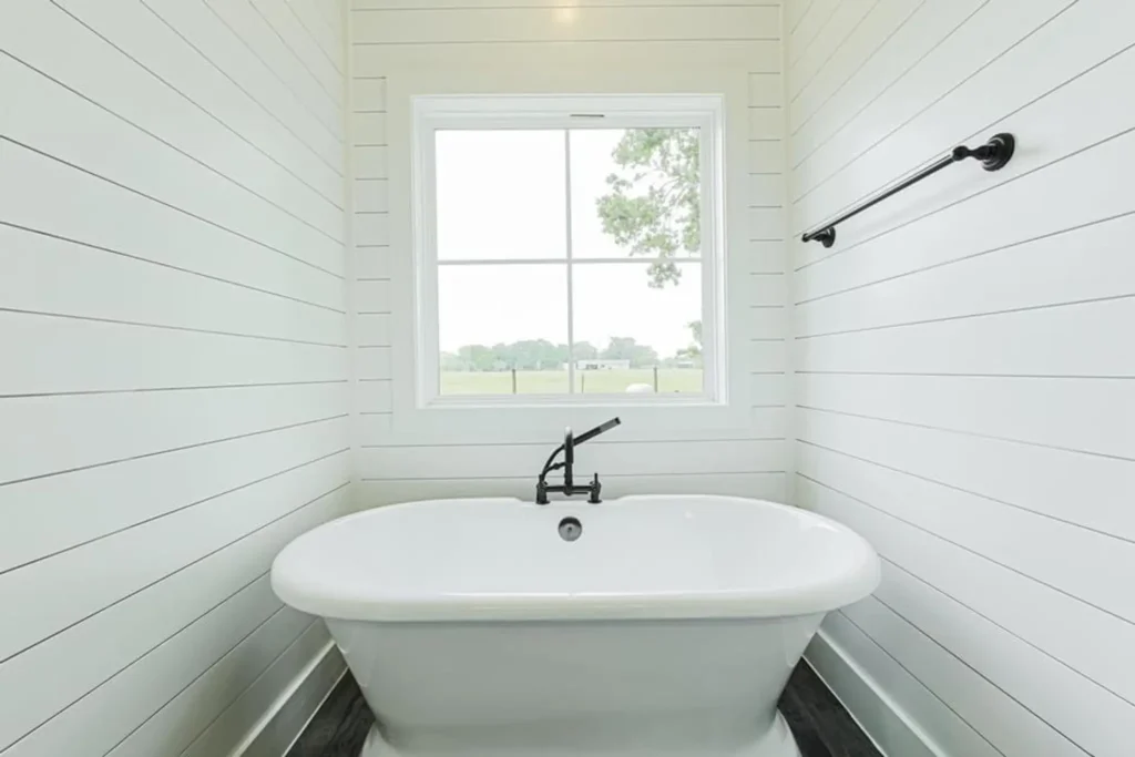 Custom home bathroom with a freestanding soaking tub against a white shiplap wall