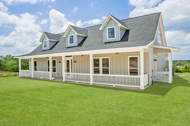 Custom-built cream single-story home with dormers and a white-railed front porch