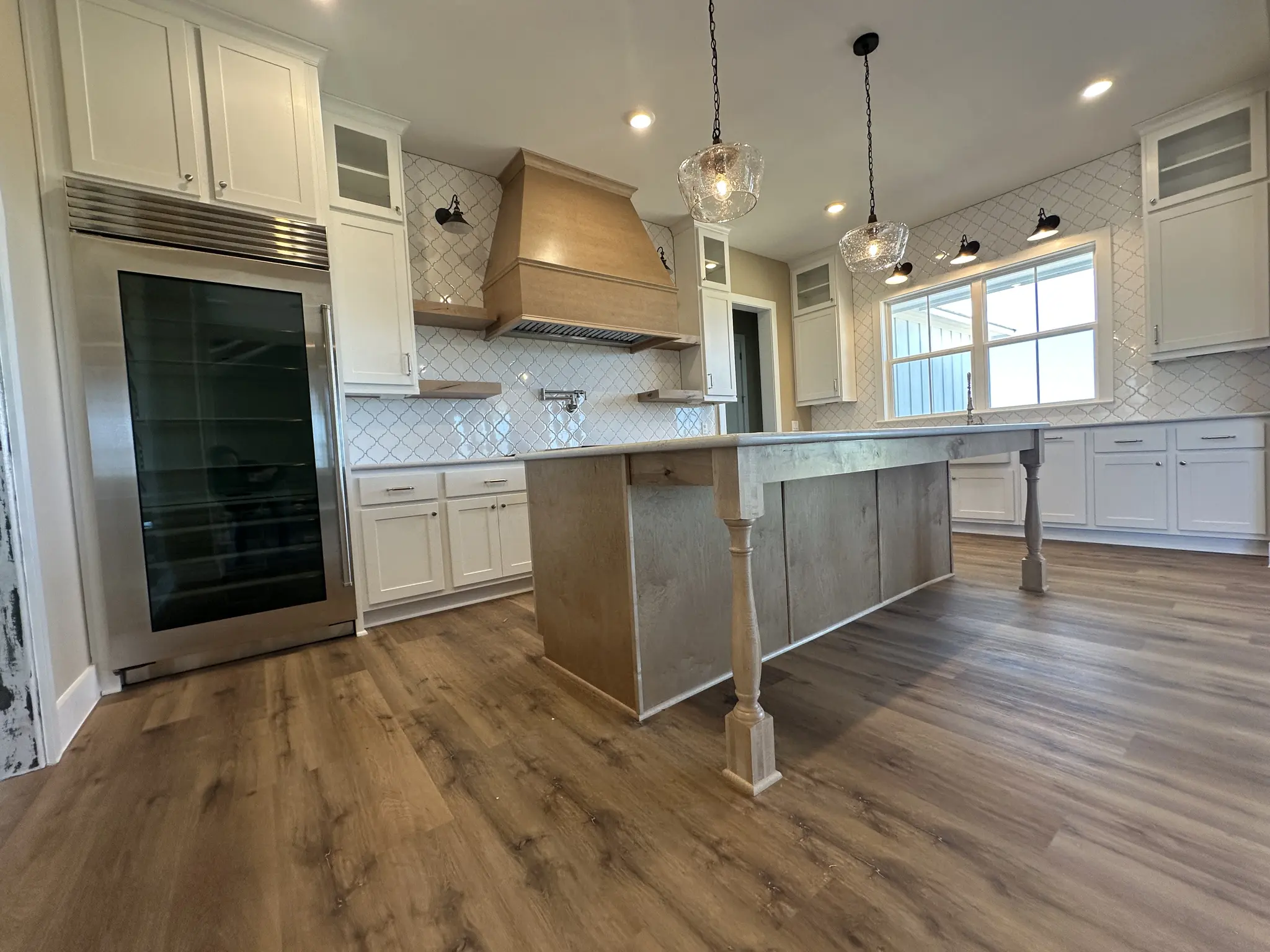 Open-concept custom home kitchen with a center island, wood range hood and pendant lights