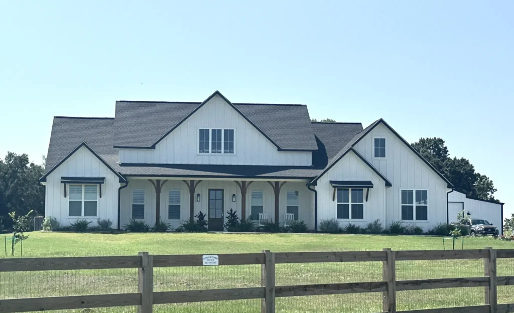 Two-story white modern farmhouse custom home with a covered porch and split-rail fence