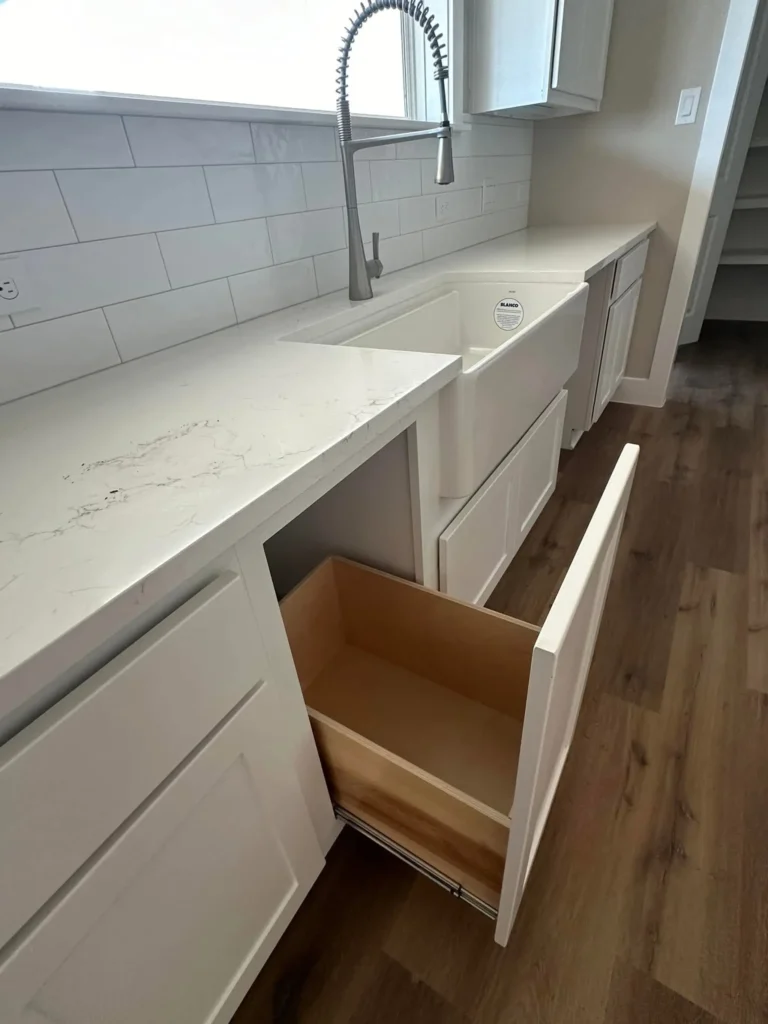 Custom home kitchen with white cabinetry, quartz counters and a pull-out storage drawer