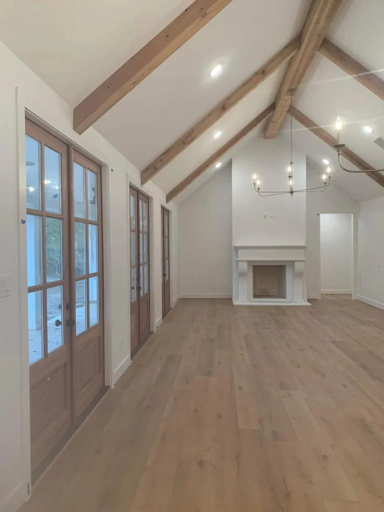 Custom home interior with a vaulted beam ceiling and French doors leading to a fireplace