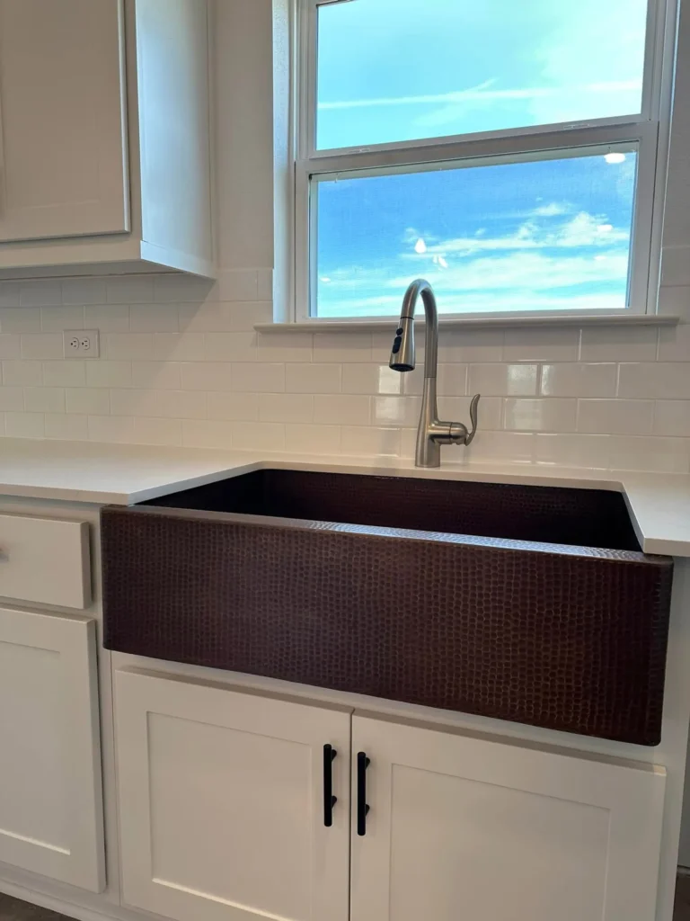 Hammered copper farmhouse apron sink with a gooseneck faucet in a custom home kitchen