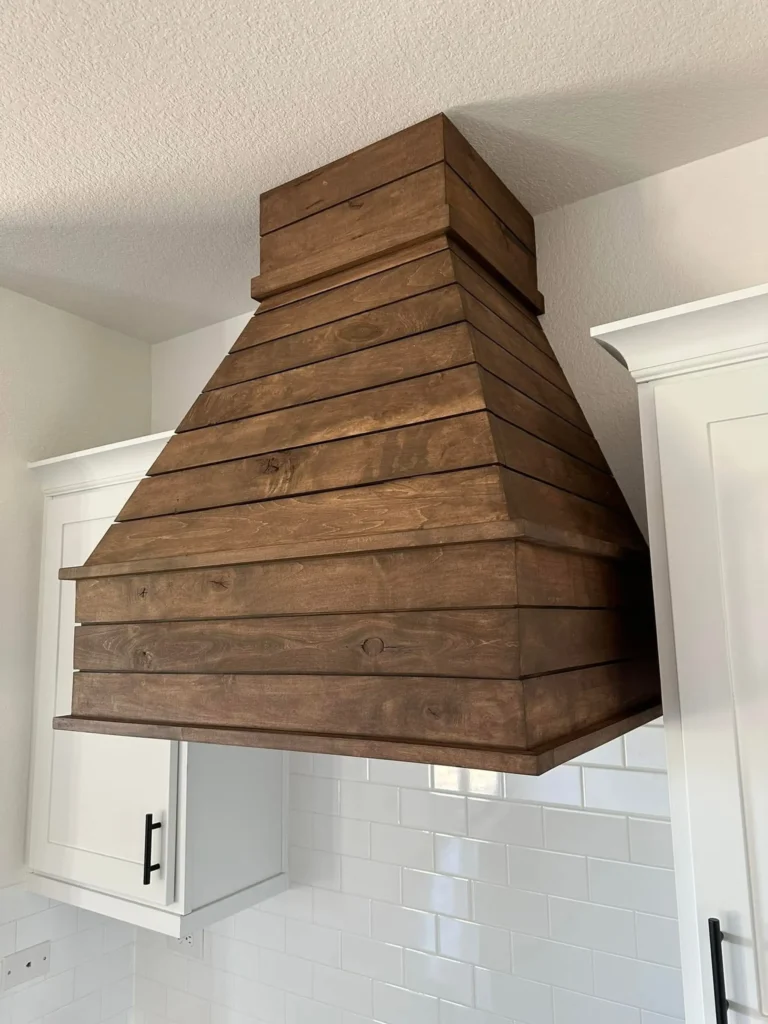 Custom wood range hood above the stove with a subway tile backsplash in a custom home kitchen