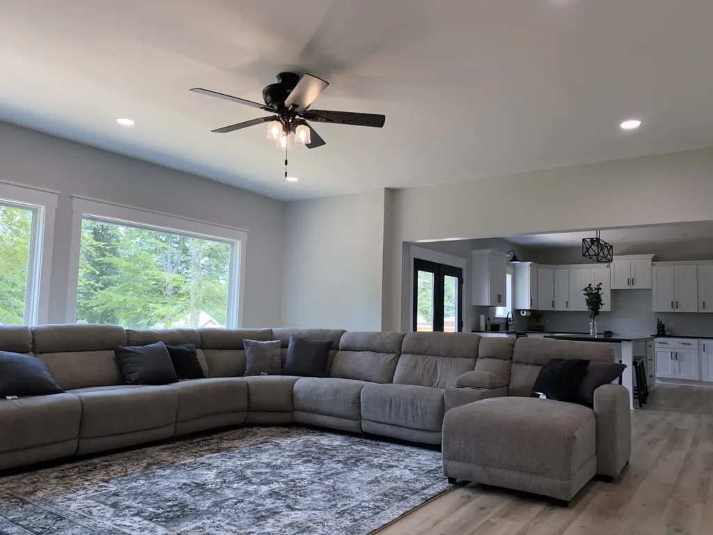 Custom home living room with a gray sectional sofa, ceiling fan and large windows