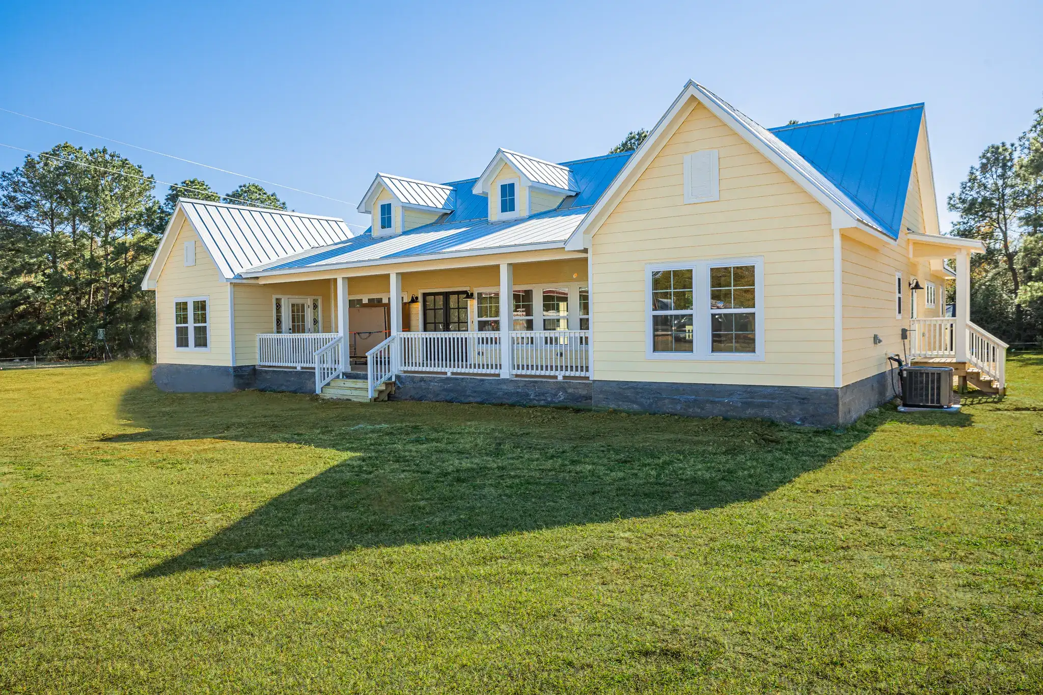 Custom-built cream farmhouse with a metal roof and covered front porch on a green lawn
