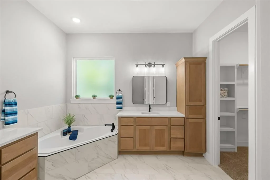 Custom home bathroom with a soaking tub beneath a window and a wood linen cabinet
